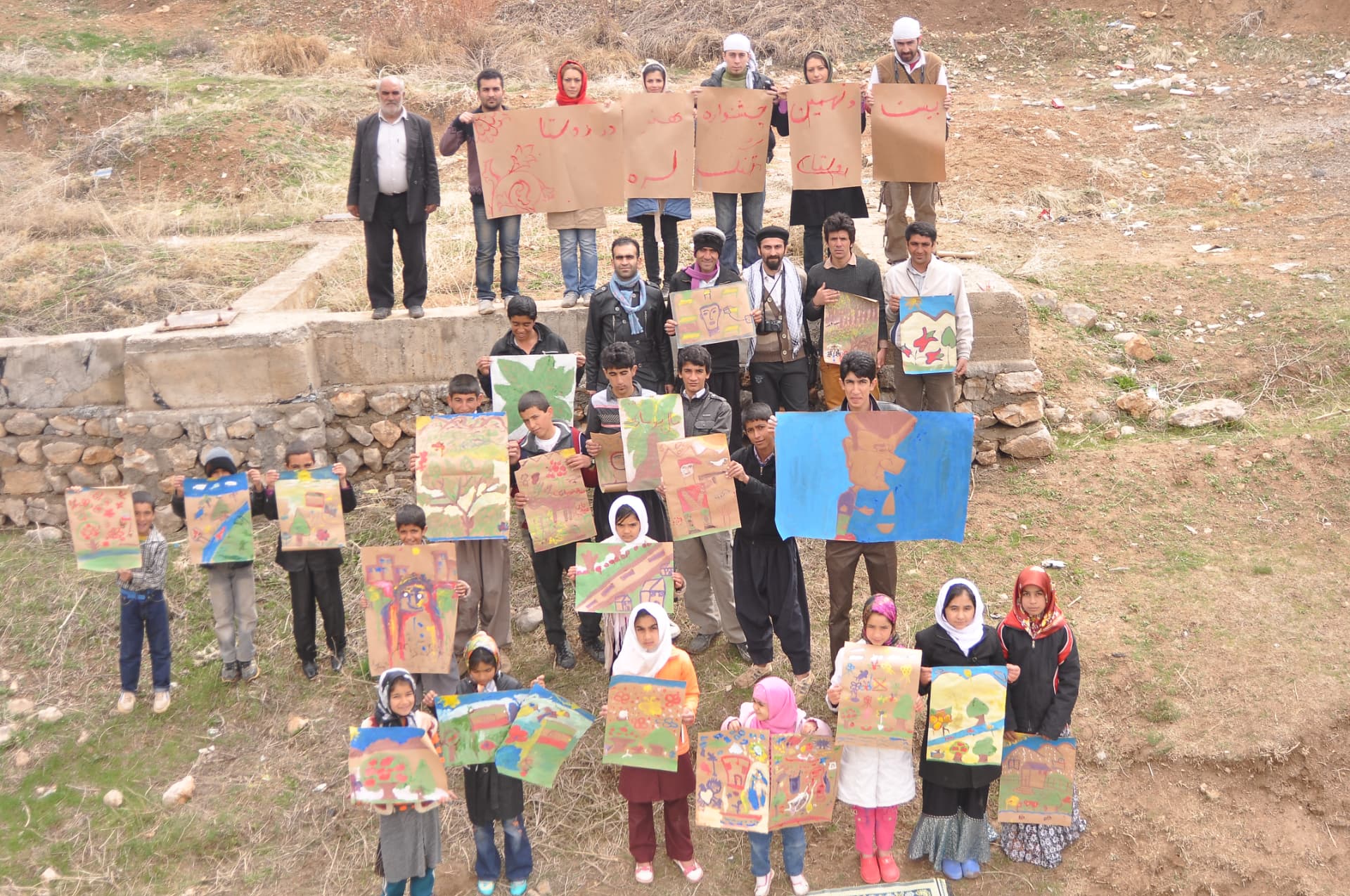 Villagers and children holding their paintings at a collective open-air exhibition in Arou Village, Damavand County